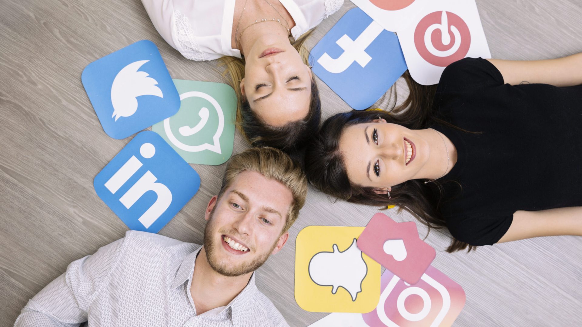 high-angle-view-friends-lying-wooden-floor-with-social-media-icons